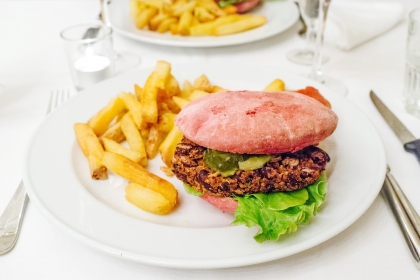 Burger de quinoa et de haricots rouges dans un petit pain aux betteraves rouges, oignons frits, chips d’aneth et salsa verde