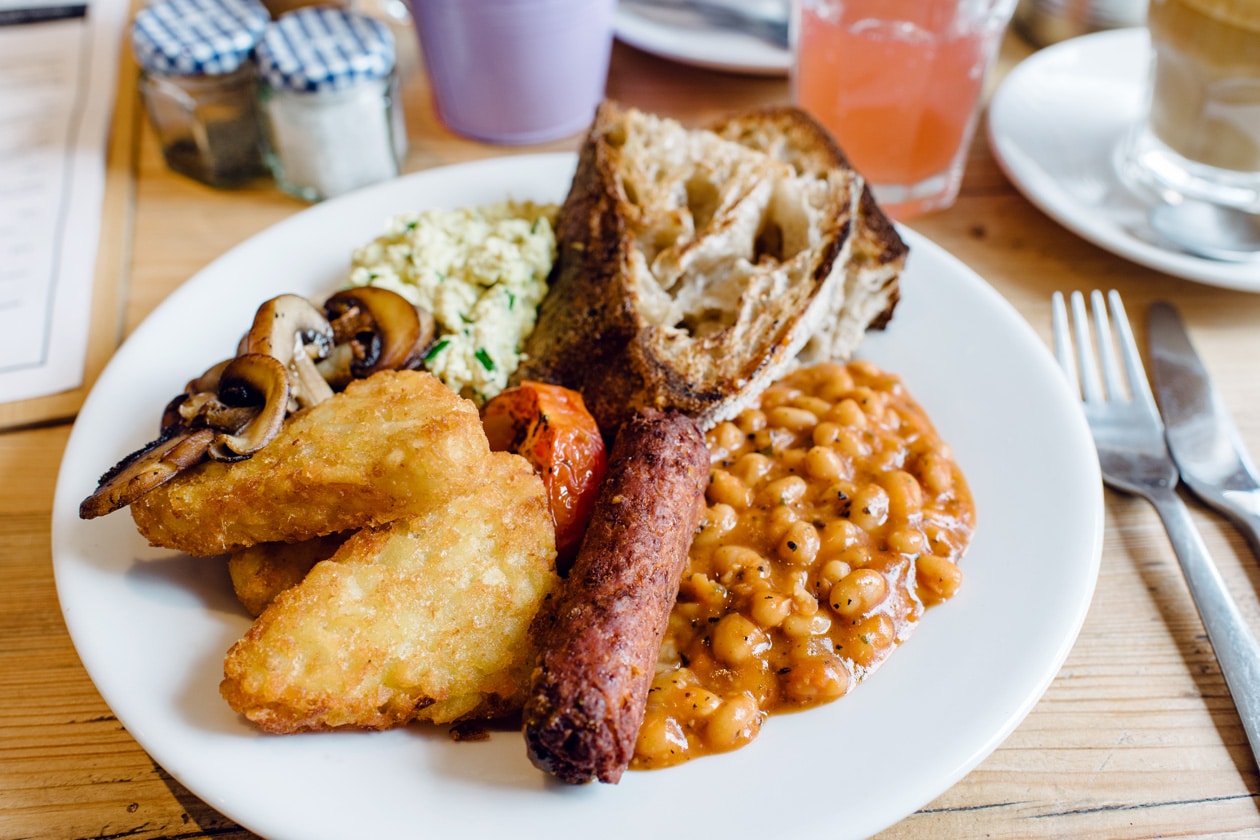 Repas végétalien au café The Canvas à Londres: Full English Breakfast avec du tofu brouillé, une saucisse végétale, des haricots blancs à la sauce tomate, des champignons et des tomates rôties, des croquettes de pommes de terre et du pain grillé