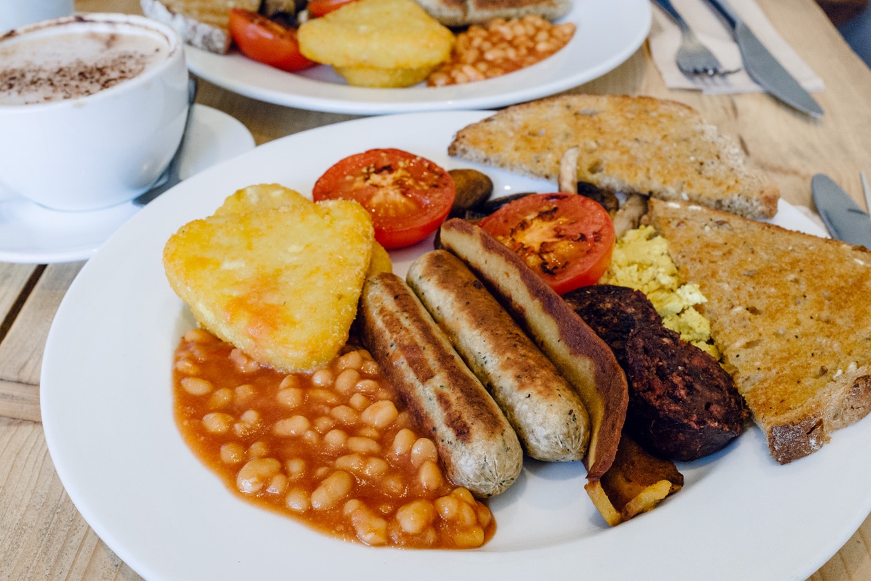 Repas végétalien au Green Kitchen Vegan Cafe à Brighton: Full English Breakfast avec du tofu brouillé, deux saucisses végétale, du bacon végétal, deux morceaux de black pudding, des haricots blancs à la sauce tomate et des tomates rôties, des croquettes de pommes de terre et du pain grillé